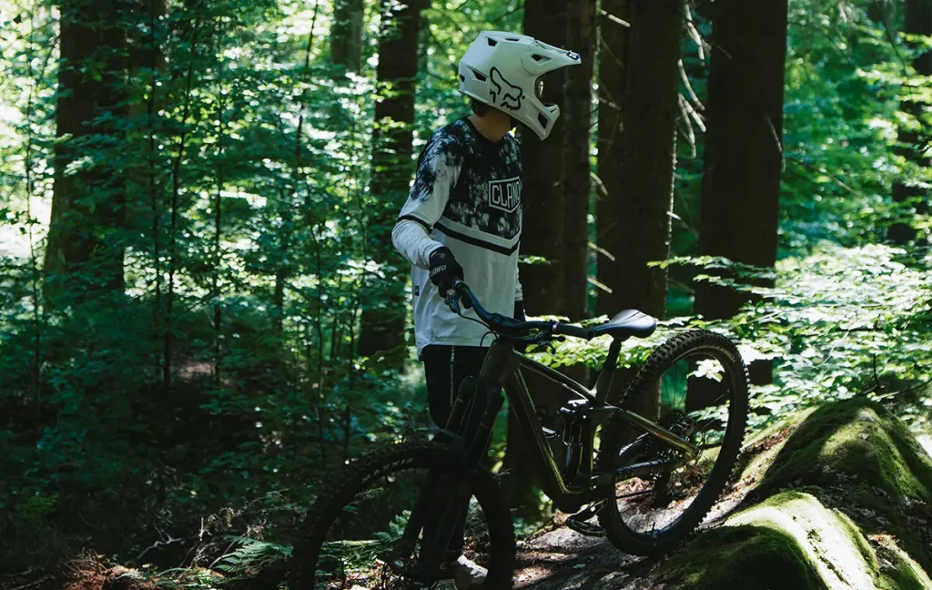 Mountainbiker steht mit seinem Bike zwischen moosbewachsenen Felsen im Wald.