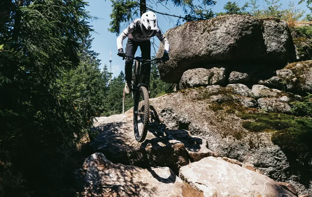 Mountainbiker springt mit angehobenem Vorderrad über eine Felssektion auf dem fOXtrott.