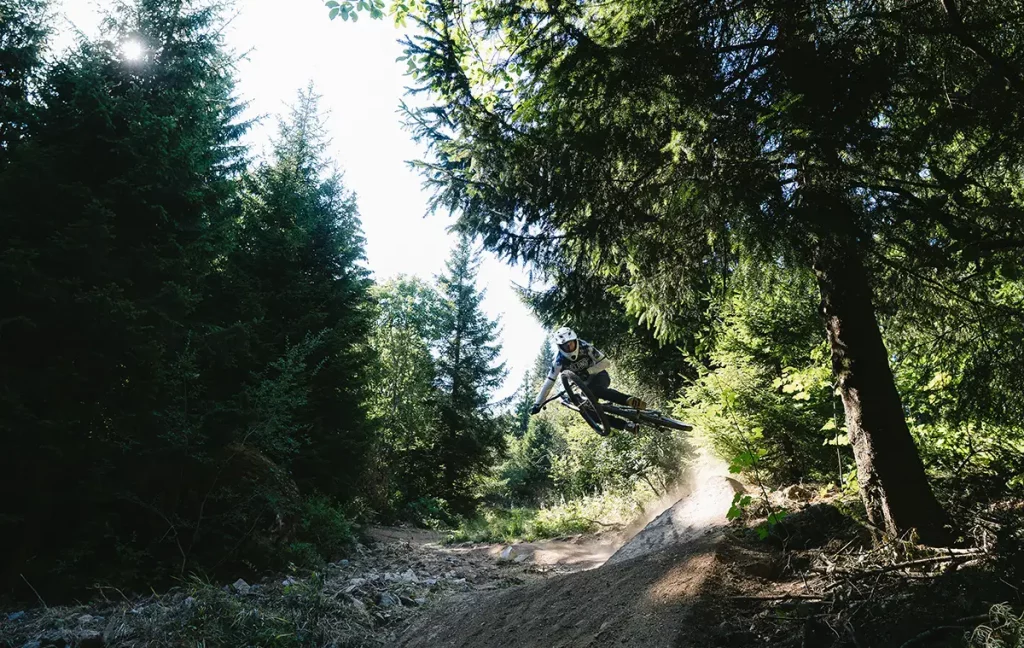 Mountainbiker fährt über eine felsige Stufe zwischen großen Granitblöcken im Wald.